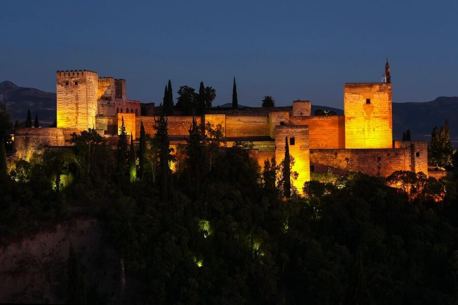 The Alhambra lit above the Darro valley at dusk, Sierra Nevada behind it